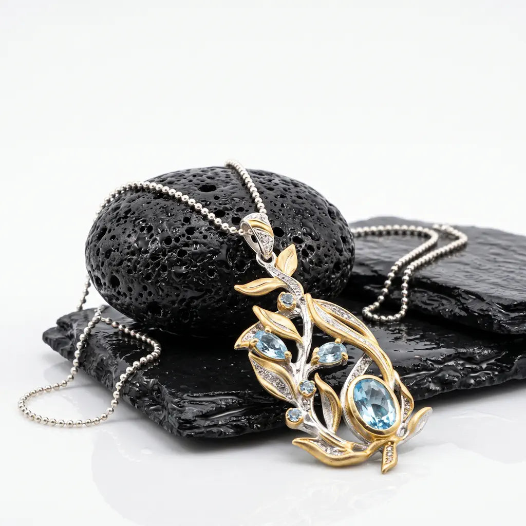 Luxus-Collier AURORA MARINA mit einer 1 mm Kugelkette, kunstvoll arrangiert auf nassem, schwarzen Lavastein zur Präsentation des floralen Blätter-Reliefs mit eisblauen Topasen.