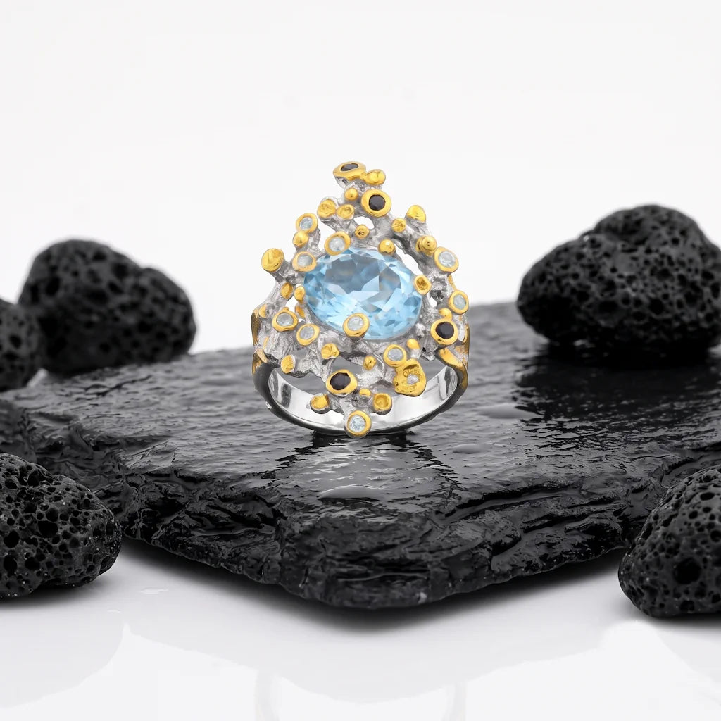 ASTRAL REEF – Breiter Bicolor Statement Ring mit blauem Topas und Saphir aus 925 Sterling Silber präsentiert auf schwarzem Lavastein von René Rose Jewelry