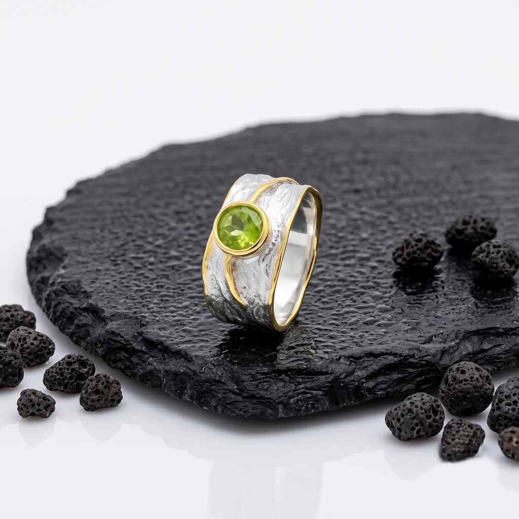 ARTEMIS – Breiter Bicolor Bandring mit grünem Peridot Edelstein aus 925 Sterling Silber präsentiert auf schwarzem Lavastein von René Rose Jewelry