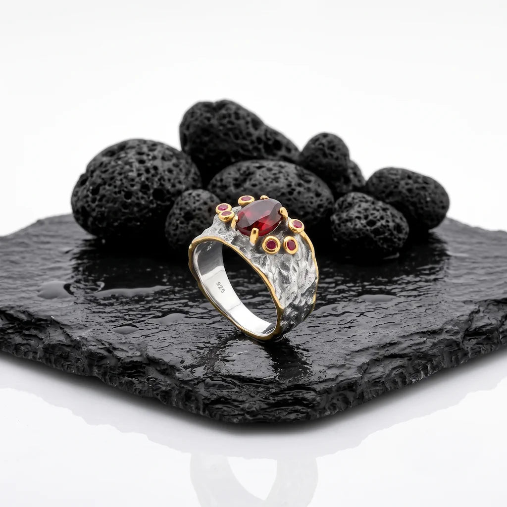 LIVIA VOLCANO – Breiter Bicolor Statement Ring mit rotem Granat und Saphir aus 925 Sterling Silber präsentiert auf schwarzem Lavastein von René Rose Jewelry