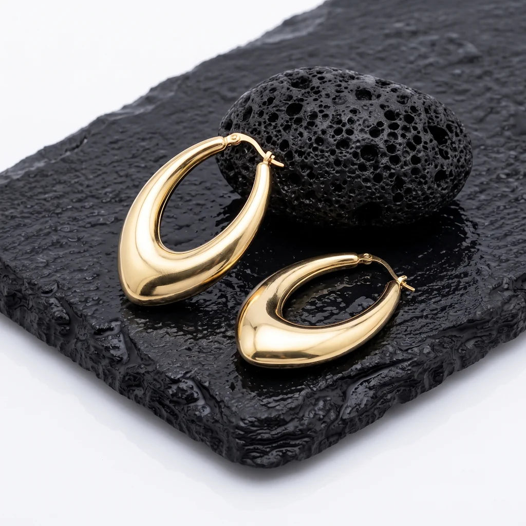 EMMA DROP – Elegante goldene Teardrop Creolen aus wasserfestem 316L Edelstahl präsentiert auf dunkler Schieferplatte von René Rose Jewelry