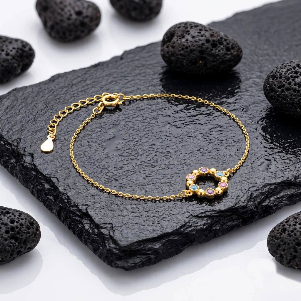 René Rose Jewelry AZURÉA luxuriöses Designer-Armband aus 925 Sterling Silber mit 14 Karat Gelbgold-Vergoldung, Kreis-Anhänger und blauen sowie lilafarbenen Zirkonia, stilvoll auf Lavastein und Schieferplatten präsentiert.