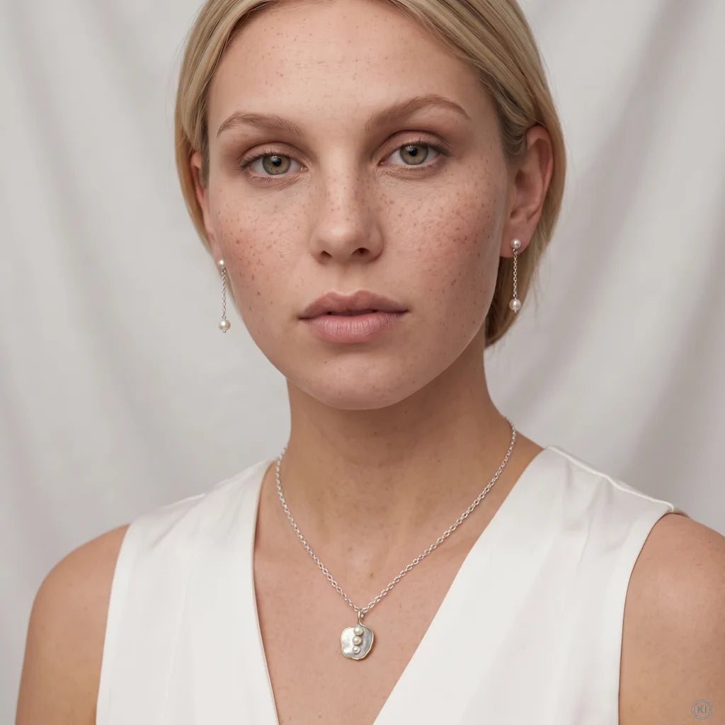 Model trägt das Bicolor XL-Collier AURA TRILOGY von René Rose Jewelry mit drei Perlen zum weißen V-Ausschnitt-Top.