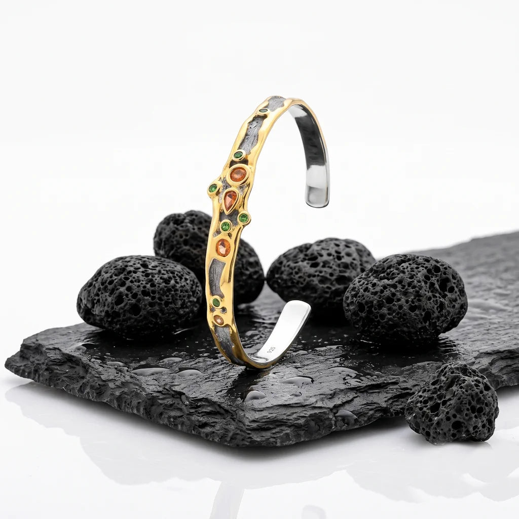 ARTEMIS CUFF – Offener Bicolor Armreif mit grünem Chromdiopsid und orangefarbenem Saphir aus 925 Sterling Silber präsentiert auf schwarzem Lavastein von René Rose Jewelry
