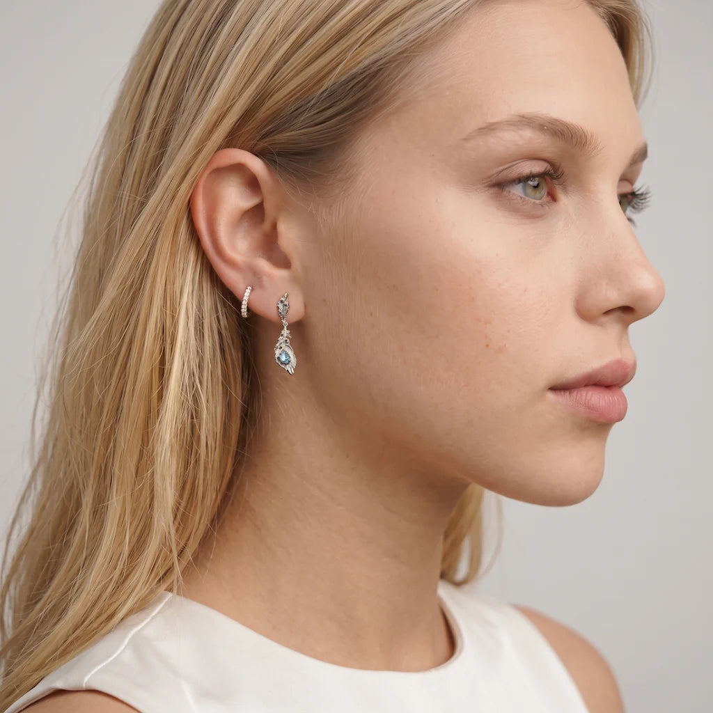 AURA FEATHER – Lange goldene Ohrringe im skulpturalen Feder Design mit blauen Edelsteinen getragen am Ohr von René Rose Jewelry