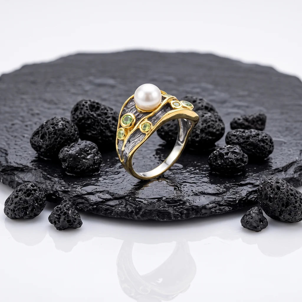 LIVIA BOUQUET – Breiter Bicolor Statement Ring mit Perle und grünem Saphir aus 925 Sterling Silber präsentiert auf schwarzem Lavastein von René Rose Jewelry