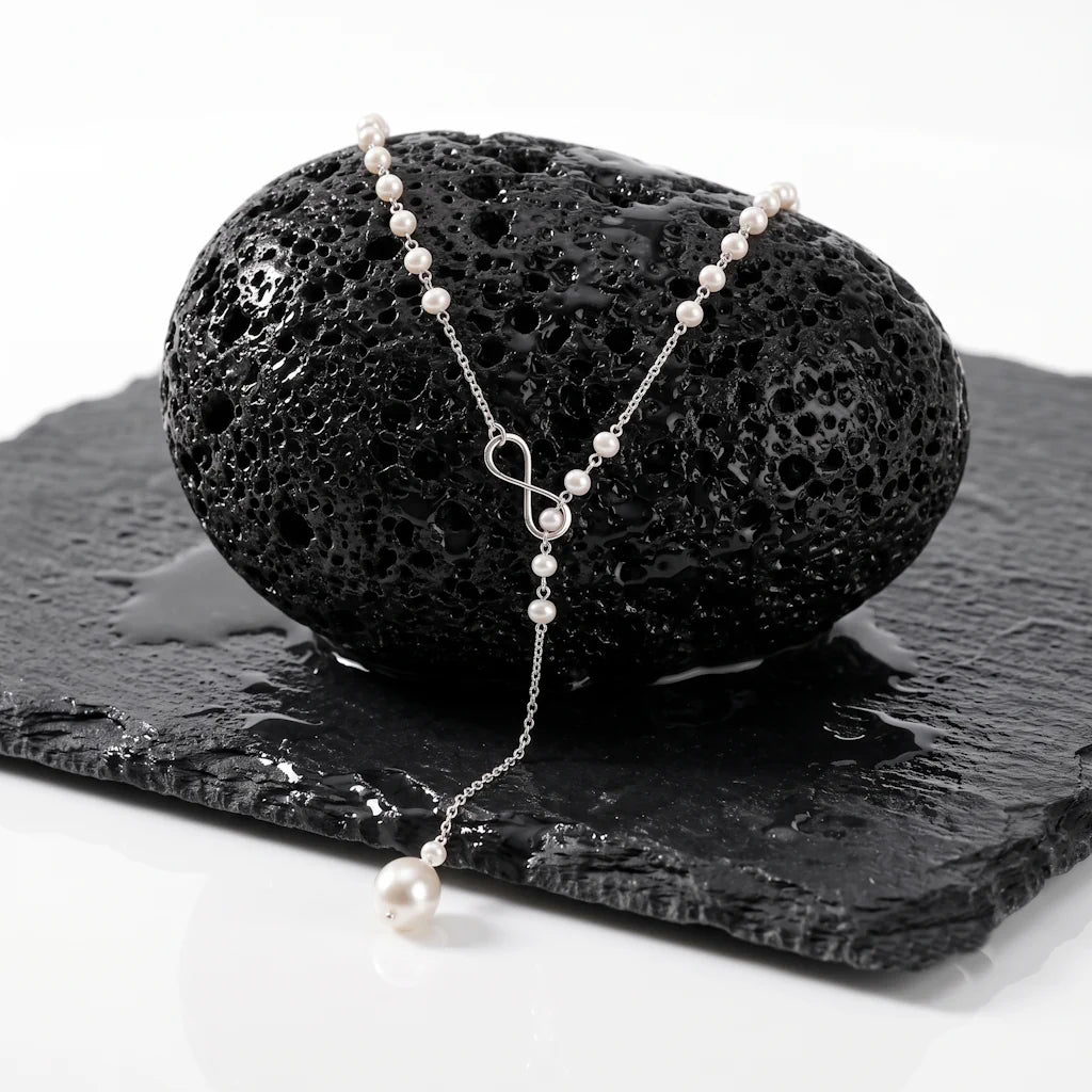 INFINITY PERLA – Filigrane Y Kette mit Infinity Symbol und echten Süßwasserperlen aus 925 Sterling Silber präsentiert auf schwarzem Lavastein von René Rose Jewelry