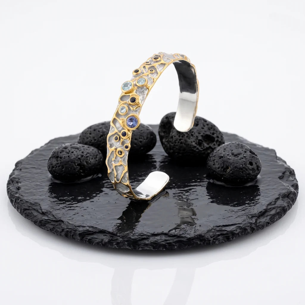 STELLA COSMICA – Breiter Manschetten Armreif mit seltenen Edelsteinen aus 925 Sterling Silber präsentiert auf schwarzem Lavastein von René Rose Jewelry