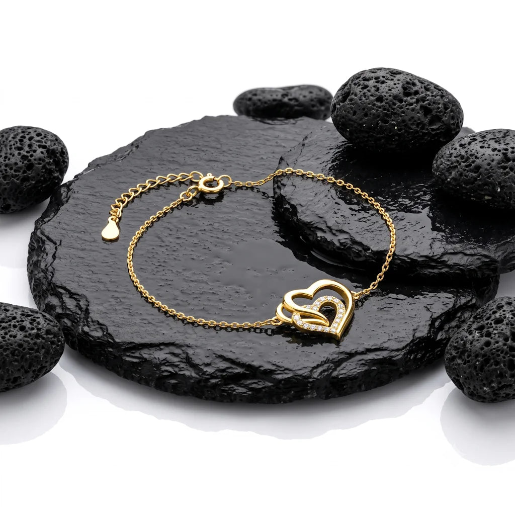 René Rose Jewelry AMORÉA luxuriöses Designer-Armband aus 925 Sterling Silber mit dreifachem Herz, weißen Zirkonia, 14 Karat Gelbgold-Vergoldung und E-Coating, stilvoll auf Lavastein und Schieferplatten präsentiert.
