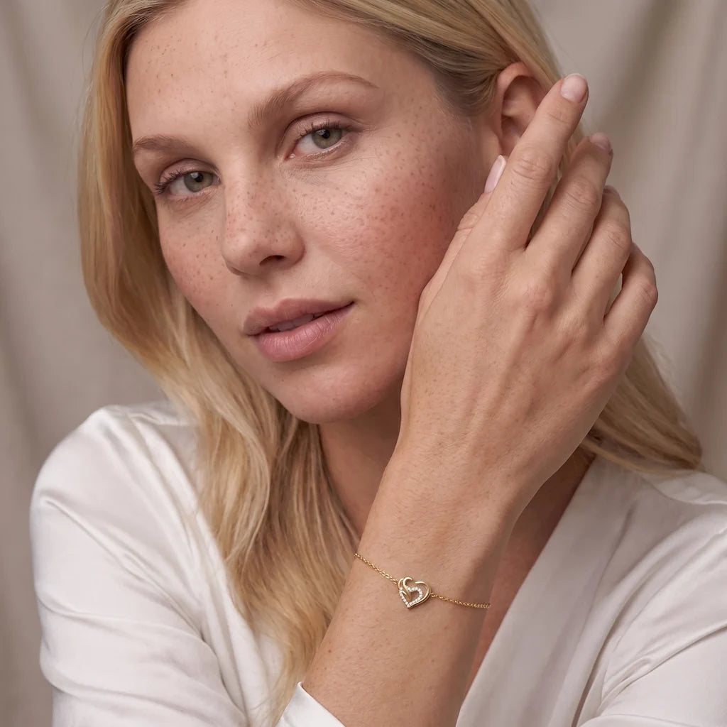 Model trägt das René Rose Jewelry AMORÉA Designer-Armband aus 925 Sterling Silber mit dreifachem Herz, weißen Zirkonia, 14 Karat Gelbgold-Vergoldung