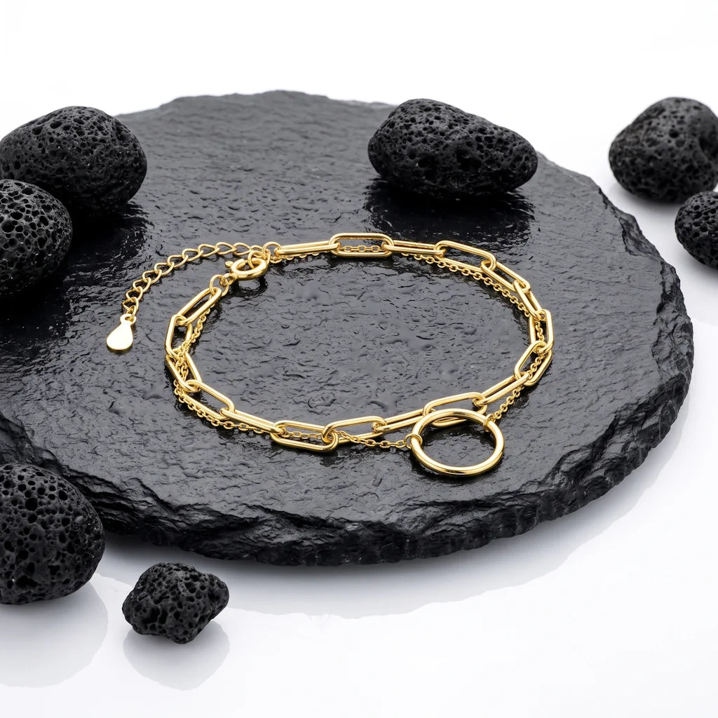 René Rose Jewelry AURELIA luxuriöses Designer-Armband aus 925 Sterling Silber mit doppelreihiger Gliederkette, Kreis-Anhänger und 14 Karat Gelbgold-Vergoldung, stilvoll auf Lavastein und Schieferplatten präsentiert.