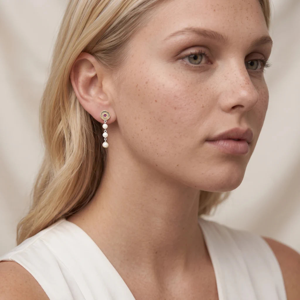 Model trägt die René Rose Jewelry AVELINE Designer-Ohrhänger aus 925 Sterling Silber mit 3 Mikron 22 Karat Gelbgold-Plattierung, Weißrhodium, Rhodolithen, echten Süßwasserperlen und Omega-Verschluss.