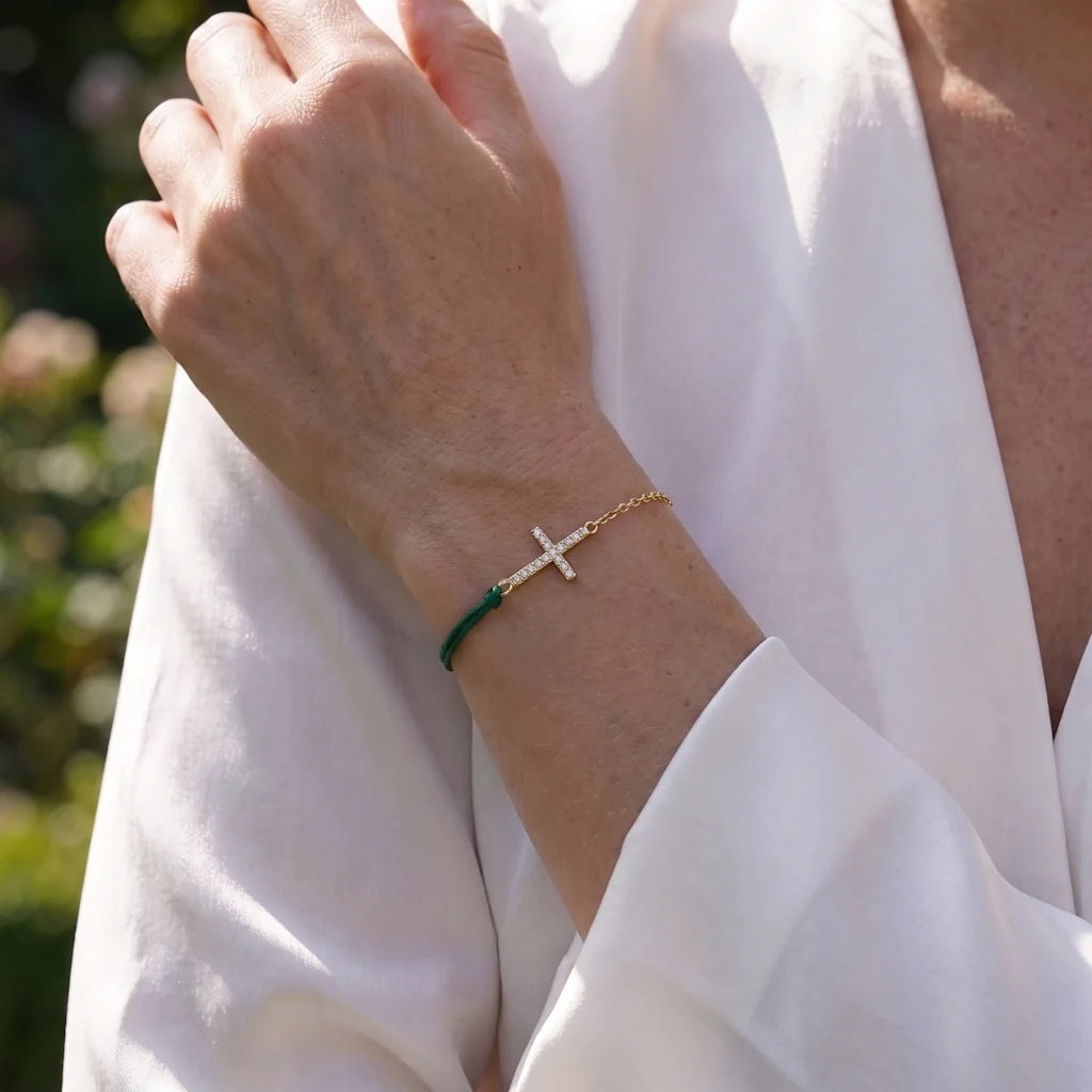 Model trägt das René Rose Jewelry SERAPHINE Designer-Armband aus 925 Sterling Silber mit vergoldetem Kreuz, weißen Zirkonia und dunkelgrüner Seidenkordel.