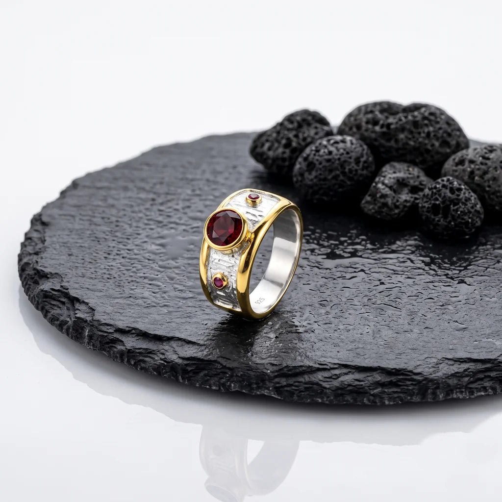 LIVIA GRANAT – Breiter Bicolor Statement Ring mit rotem Granat Edelstein aus 925 Sterling Silber präsentiert auf schwarzem Lavastein von René Rose Jewelry